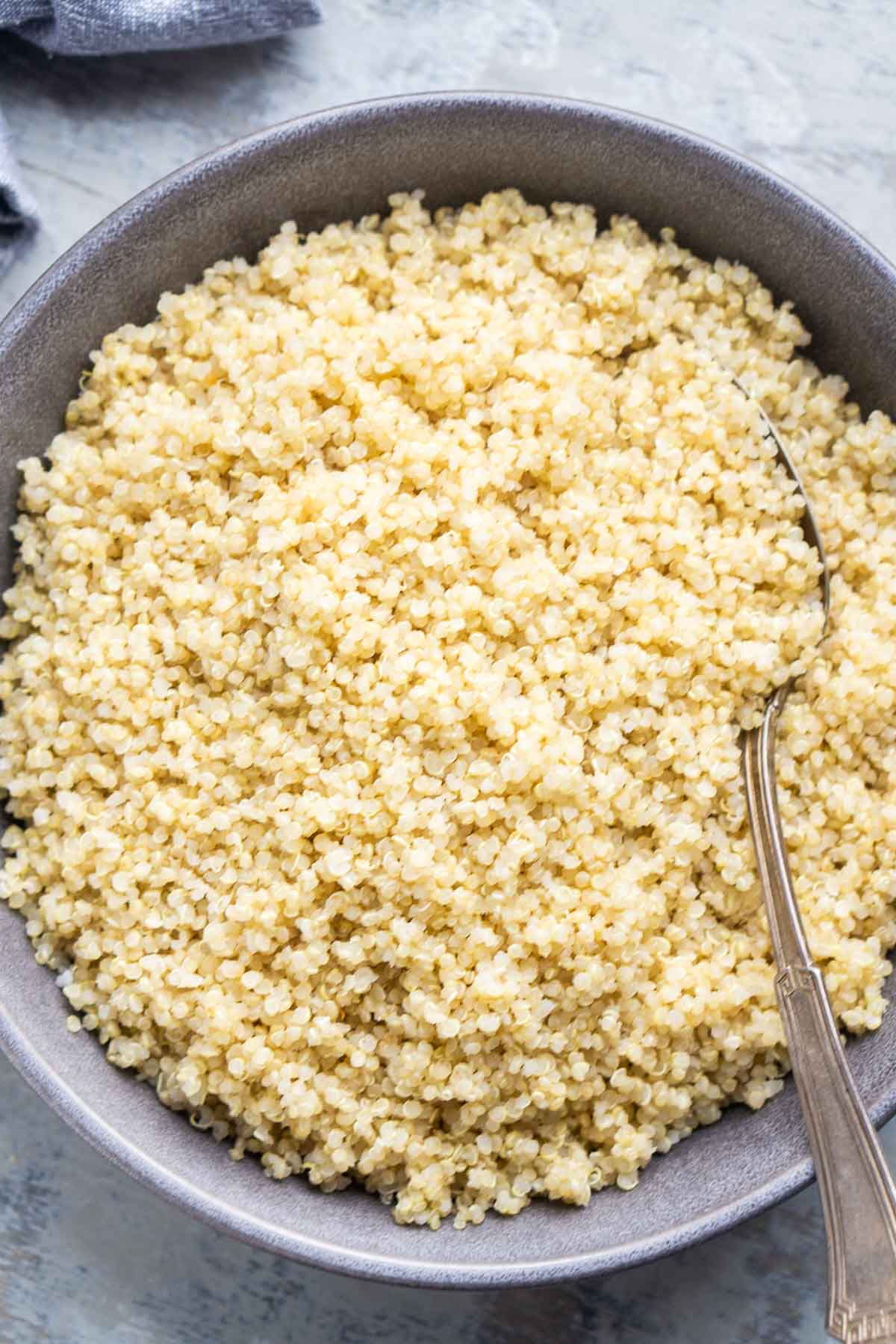 A bowl filled with cooked quinoa, with a metal spoon resting on the side.