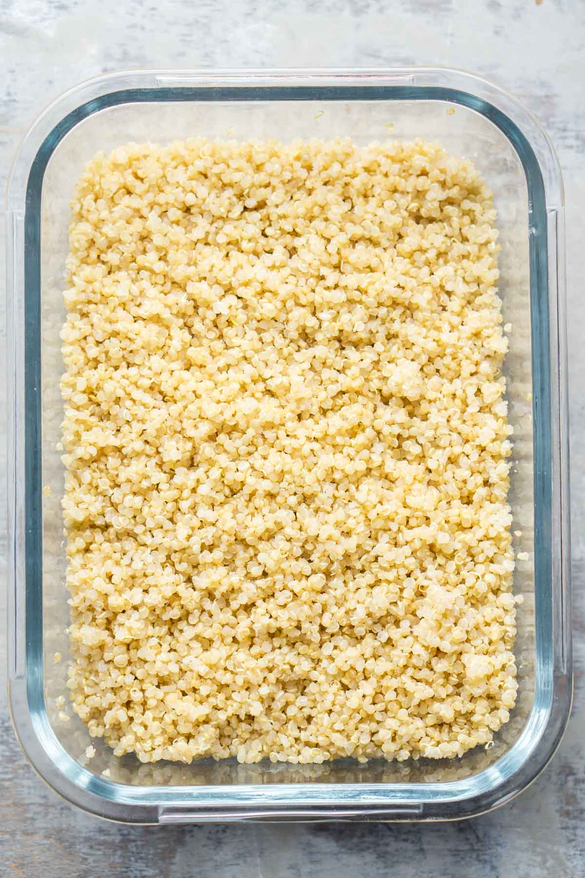A rectangular glass container filled with cooked quinoa, placed on a light-colored surface.