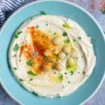 smooth and creamy hummus garnished with chickpeas, paprika, olive oil, and parsley in blue bowl