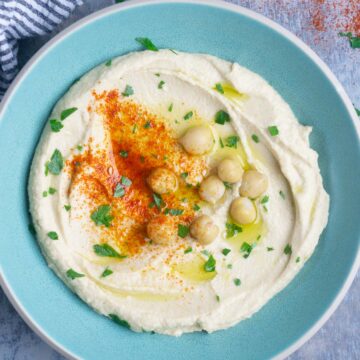 smooth and creamy hummus garnished with chickpeas, paprika, olive oil, and parsley in blue bowl