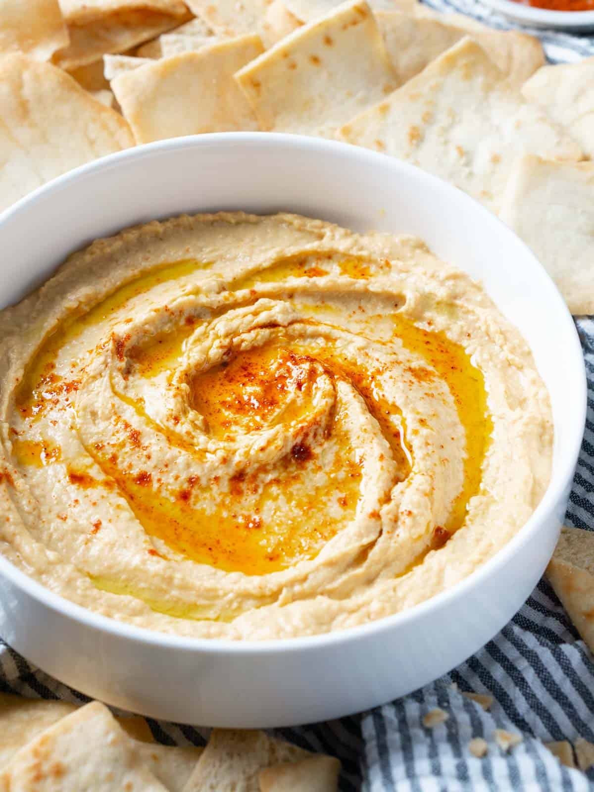 hummus garnished with olive oil and paprika in white bowl next to pita chips
