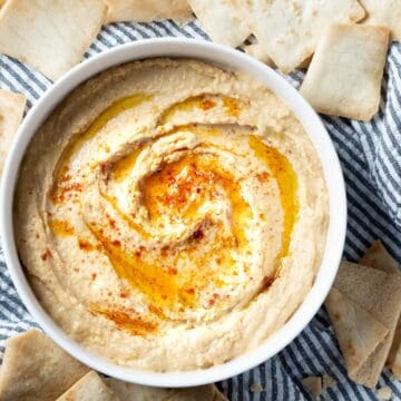 hummus garnished with olive oil and paprika in white bowl next to pita chips