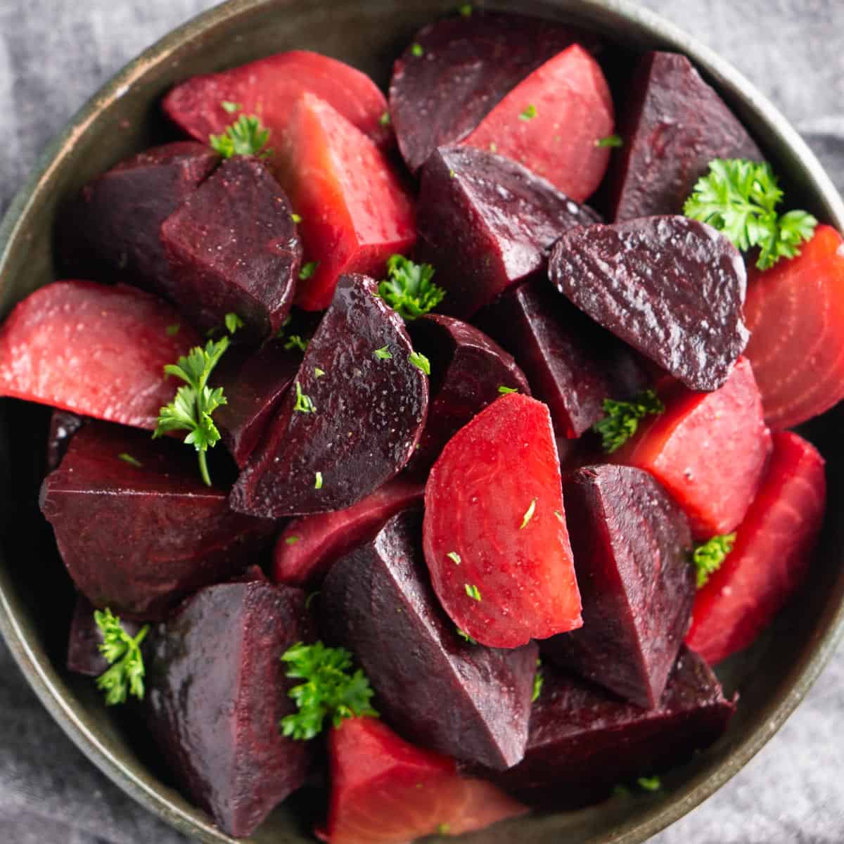 cooked beets with parsely garnish in ceramic bowl