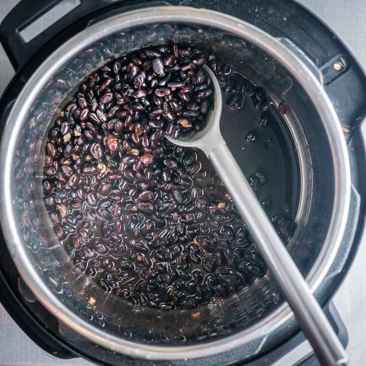 cooked black beans in Instant Pot with stirring utensil