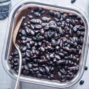 cooked black beans in glass container with silver spoon