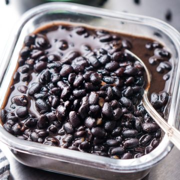 cooked black beans in glass meal prep container with silver spoon