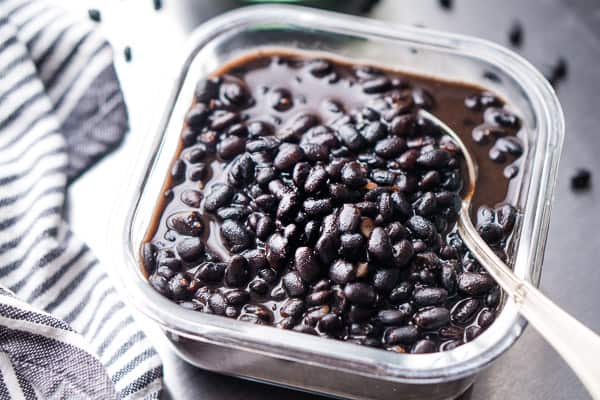 cooked black beans in glass meal prep container next to striped linen