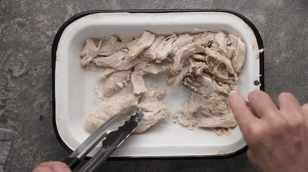 Two forks shredding chicken breast in baking pan