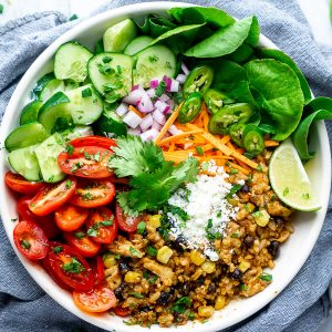 Chicken burrito bowl filling piled with fresh toppings in white bowl on blue linen