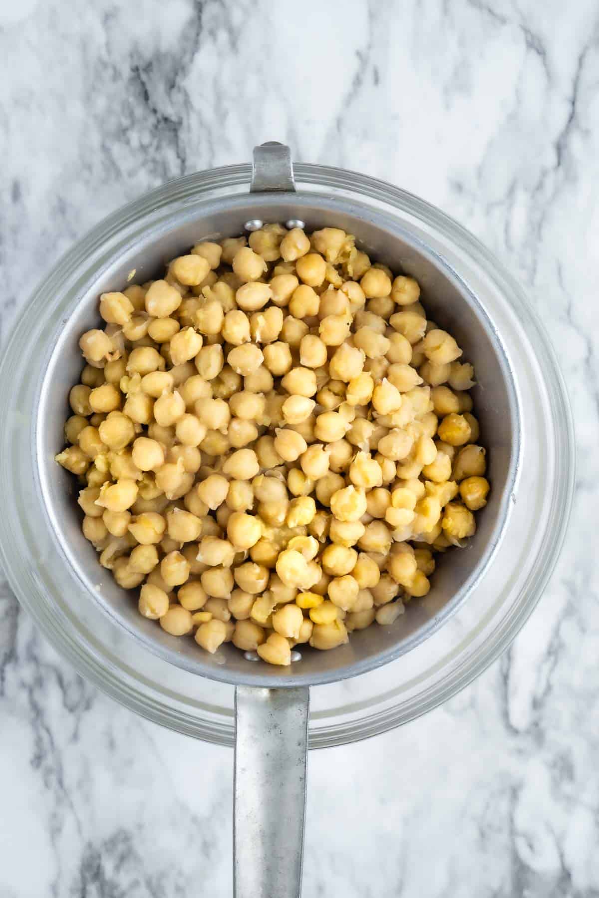 cooked chickpeas are drained in a colander over a glass mixing bowl