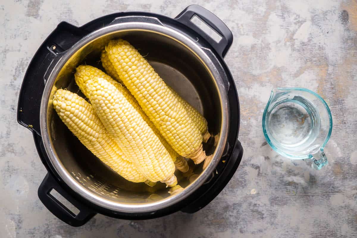 corn on the cob stacked in the Instant Pot next to measuring cup of water