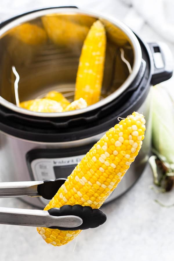 tongs Holding up a corn on the cob in front of instant pot full of corn on the cob