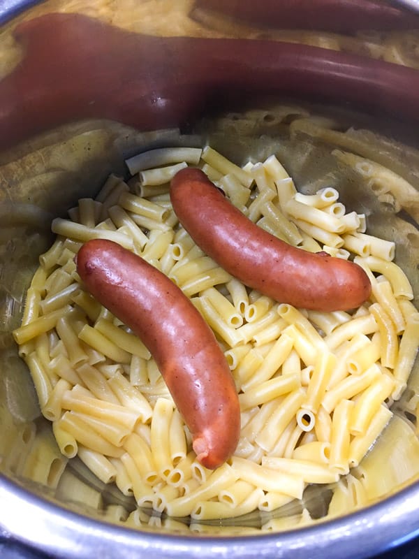 Smoked sausage links nested on top of cooked macaroni noodles in the instant pot.