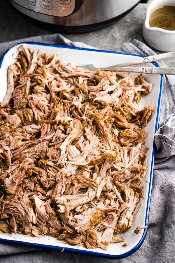 pulled pork with two pulling forks on white tray in front of Instant Pot