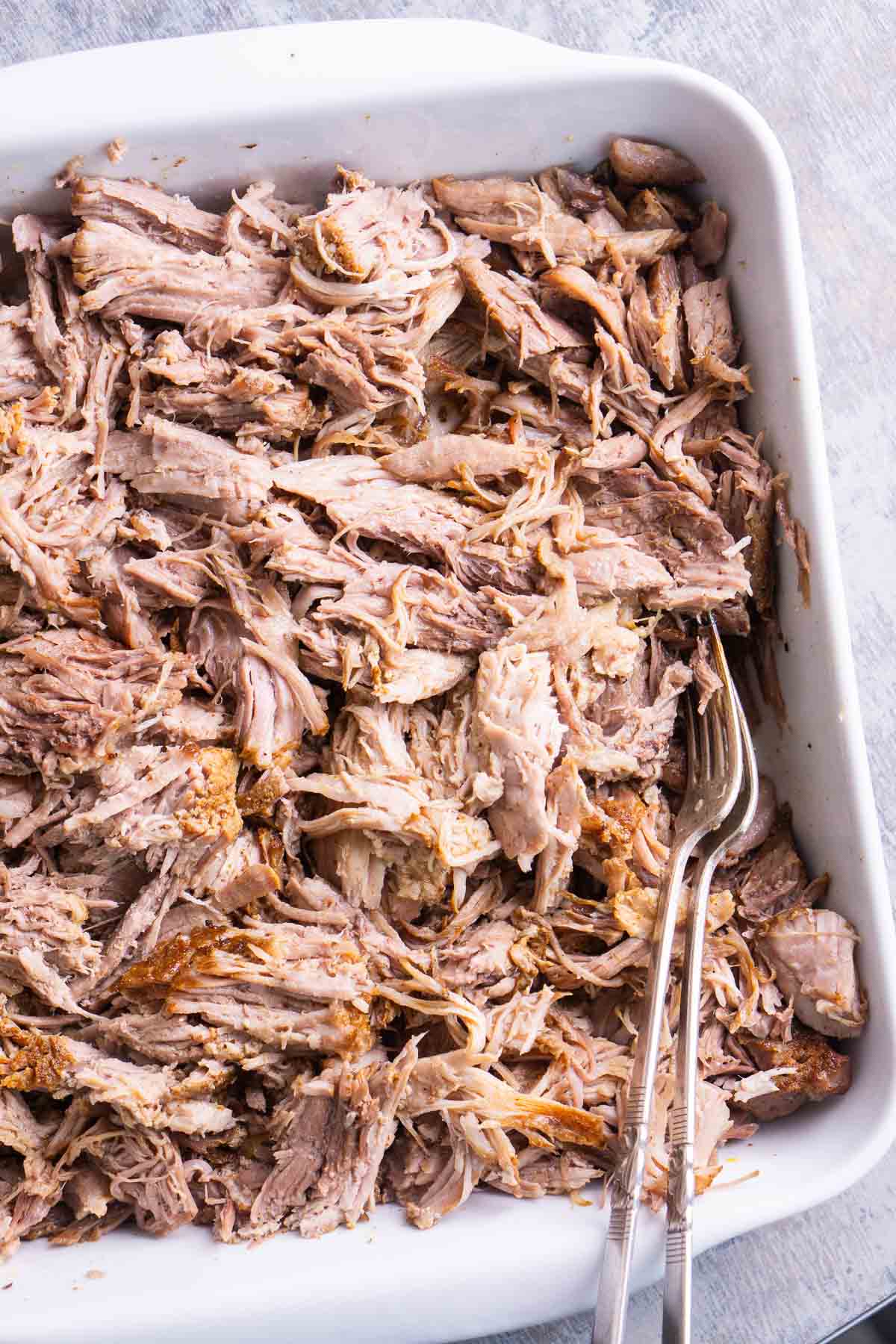 Pulled pork in white ceramic dish with two forks.