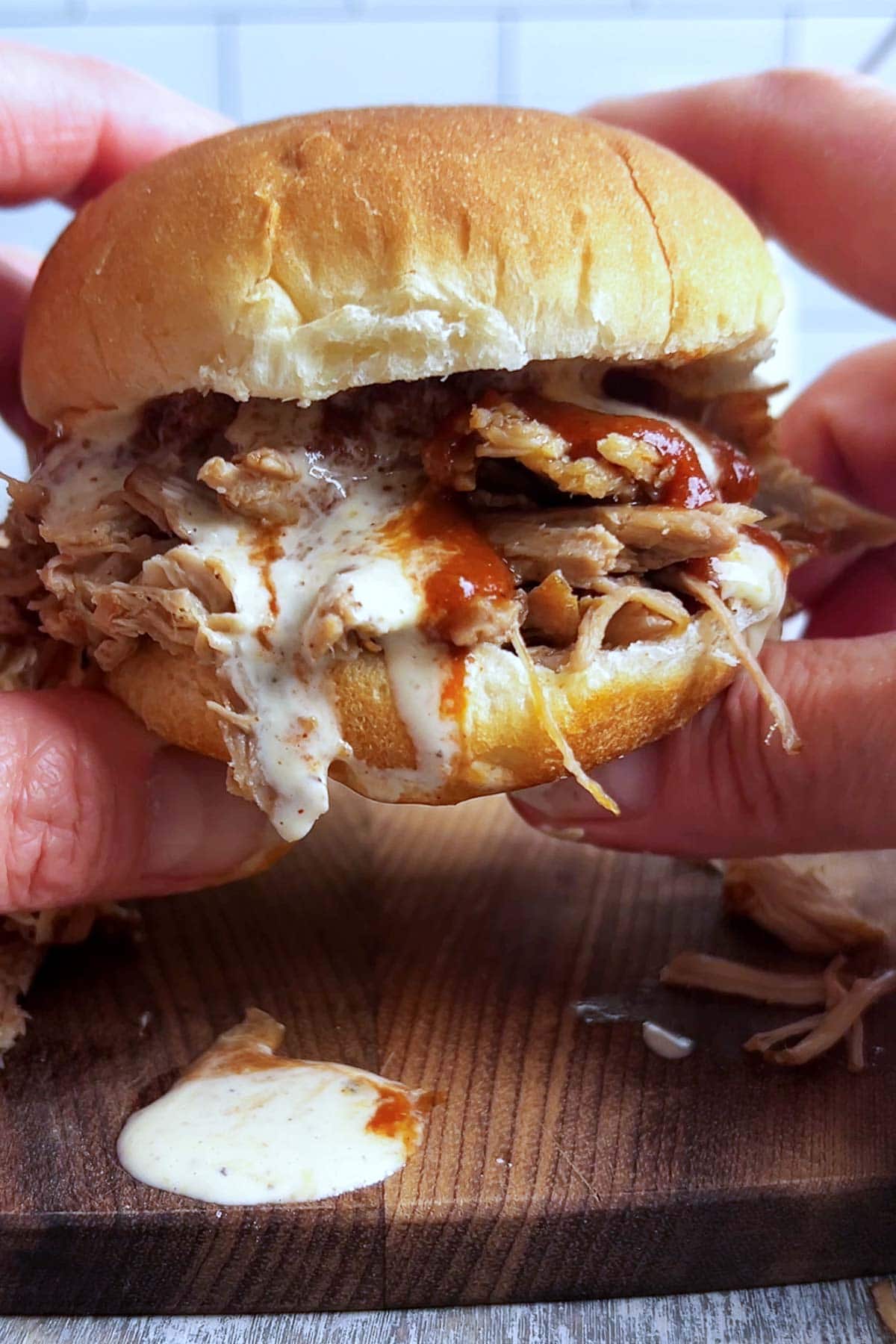 Saucy pulled pork sandwich being held by a person's hands.