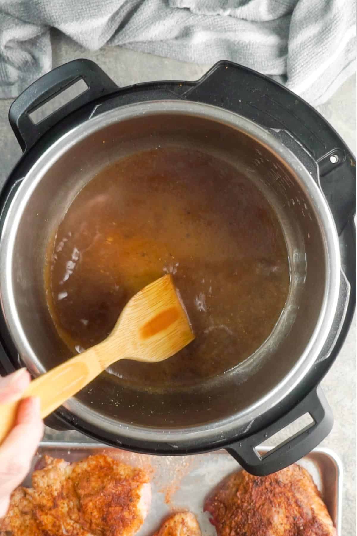 instant pot is being deglazed with a bamboo utensil
