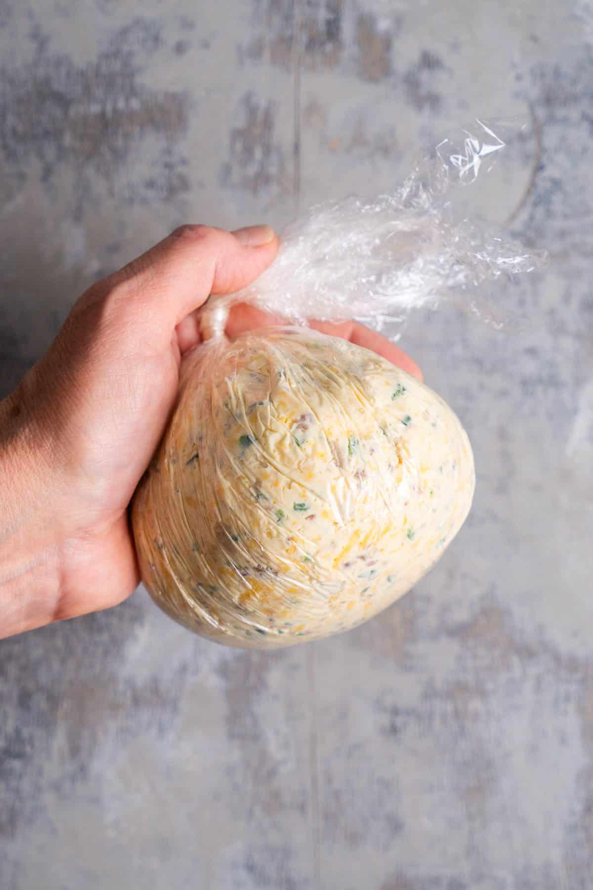person's hand holds cheese ball in plastic wrap