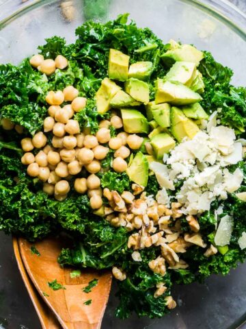 kale salad with toppings in glass bowl with salad tongs