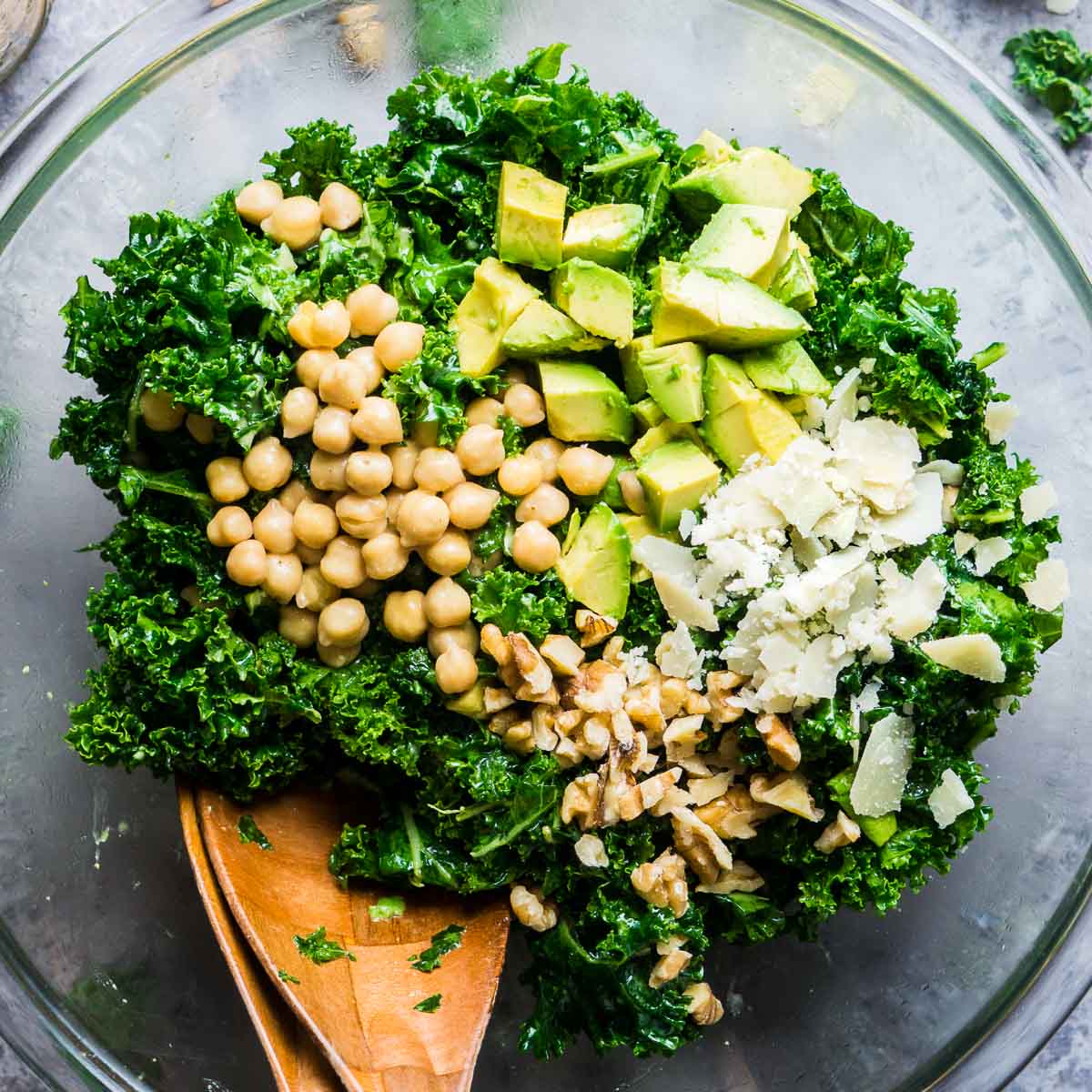 kale salad with toppings in glass bowl with salad tongs