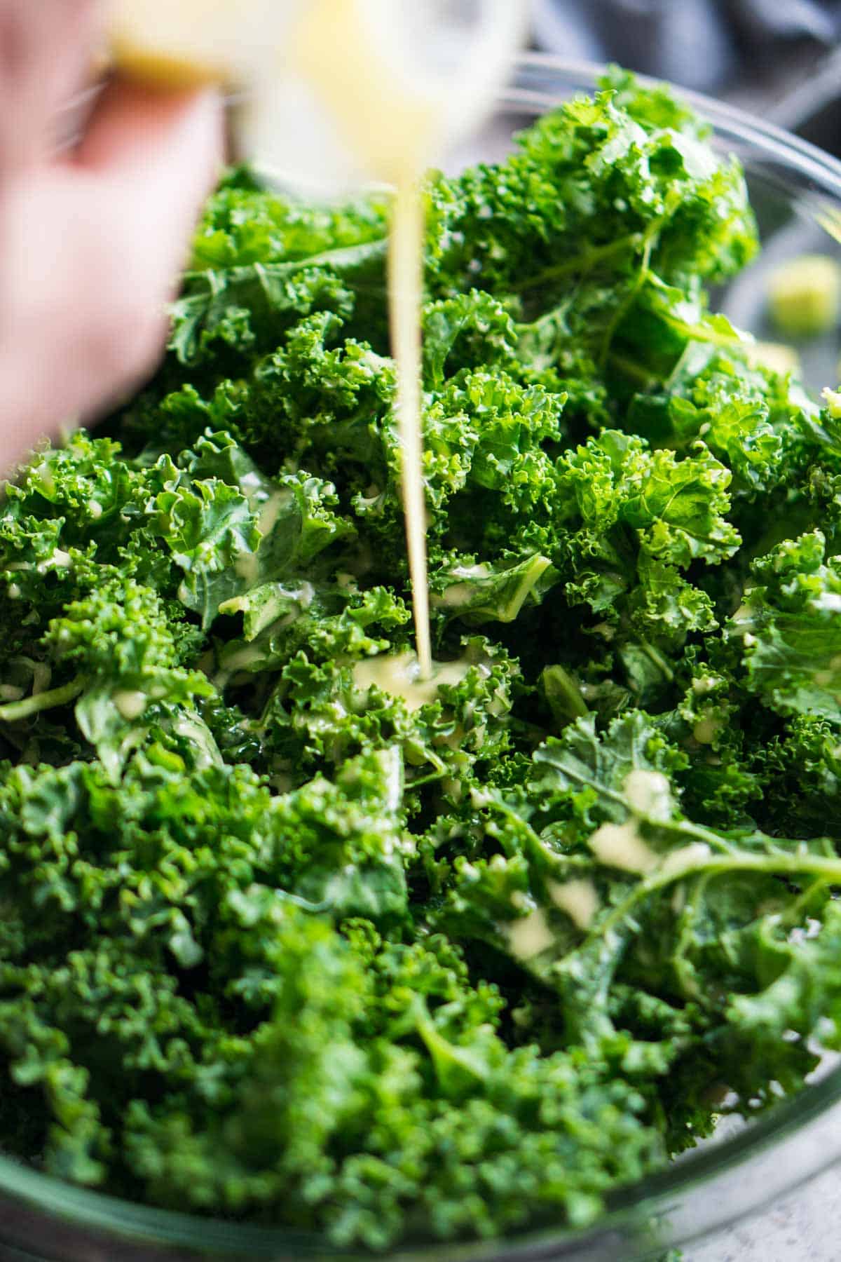 lemon dressing is added to kale in mixing bowl
