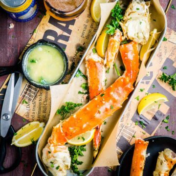 platter of king crab legs next to melted garlic butter skillet, cutting shears, and lemons