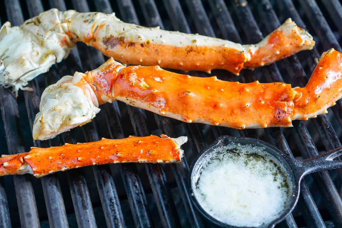 king crab legs on grill next to melted butter in mini iron skillet