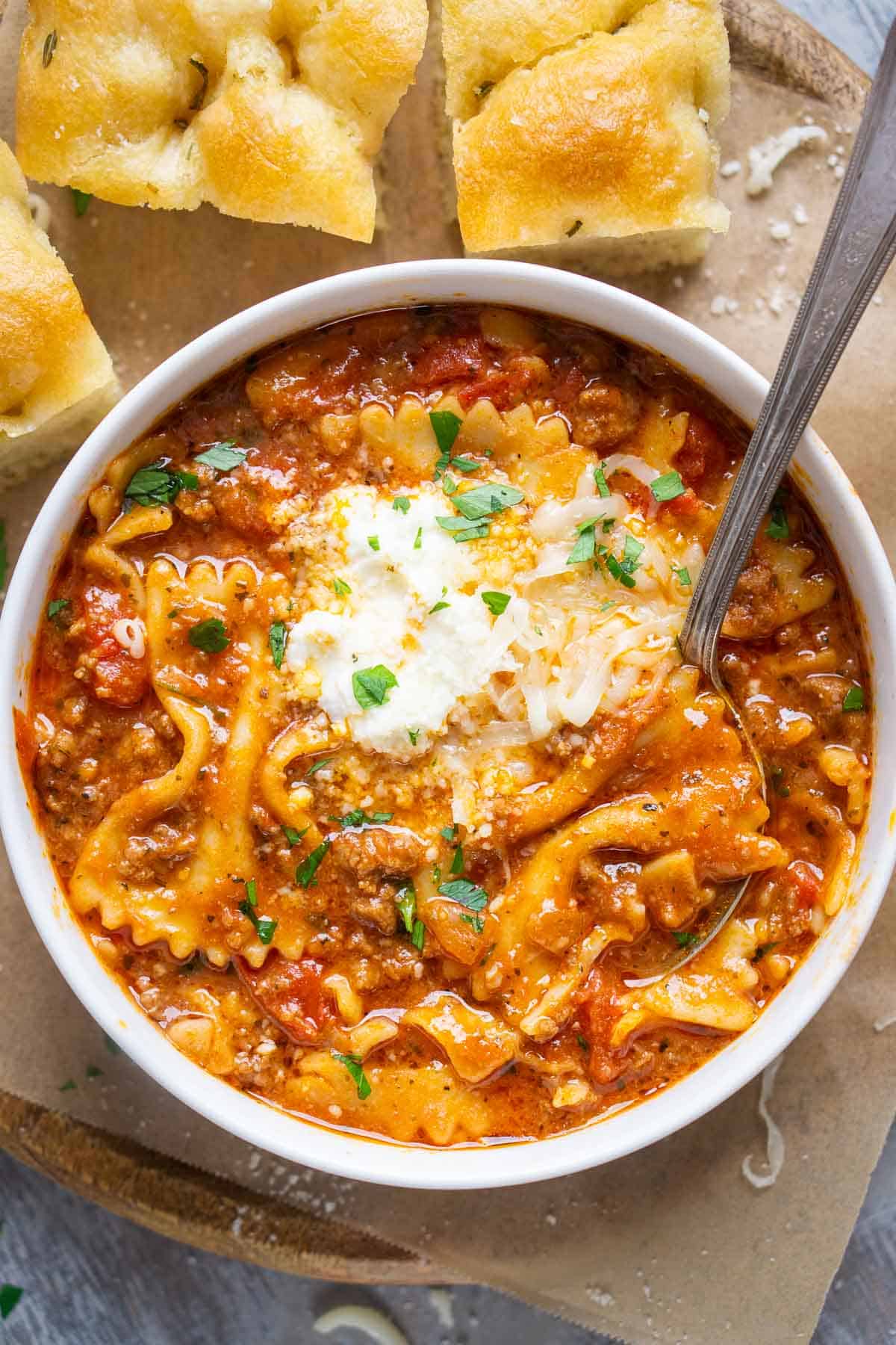 lasagna soup in white bowl with spoon next to focaccia