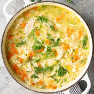 A pot of lemon chicken orzo soup with carrots, chicken breast, and fresh dill.