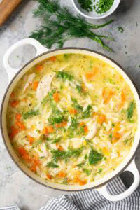 A pot of lemon chicken orzo soup with carrots, chicken breast, and fresh dill.