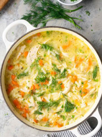 A pot of lemon chicken orzo soup with carrots, chicken breast, and fresh dill.