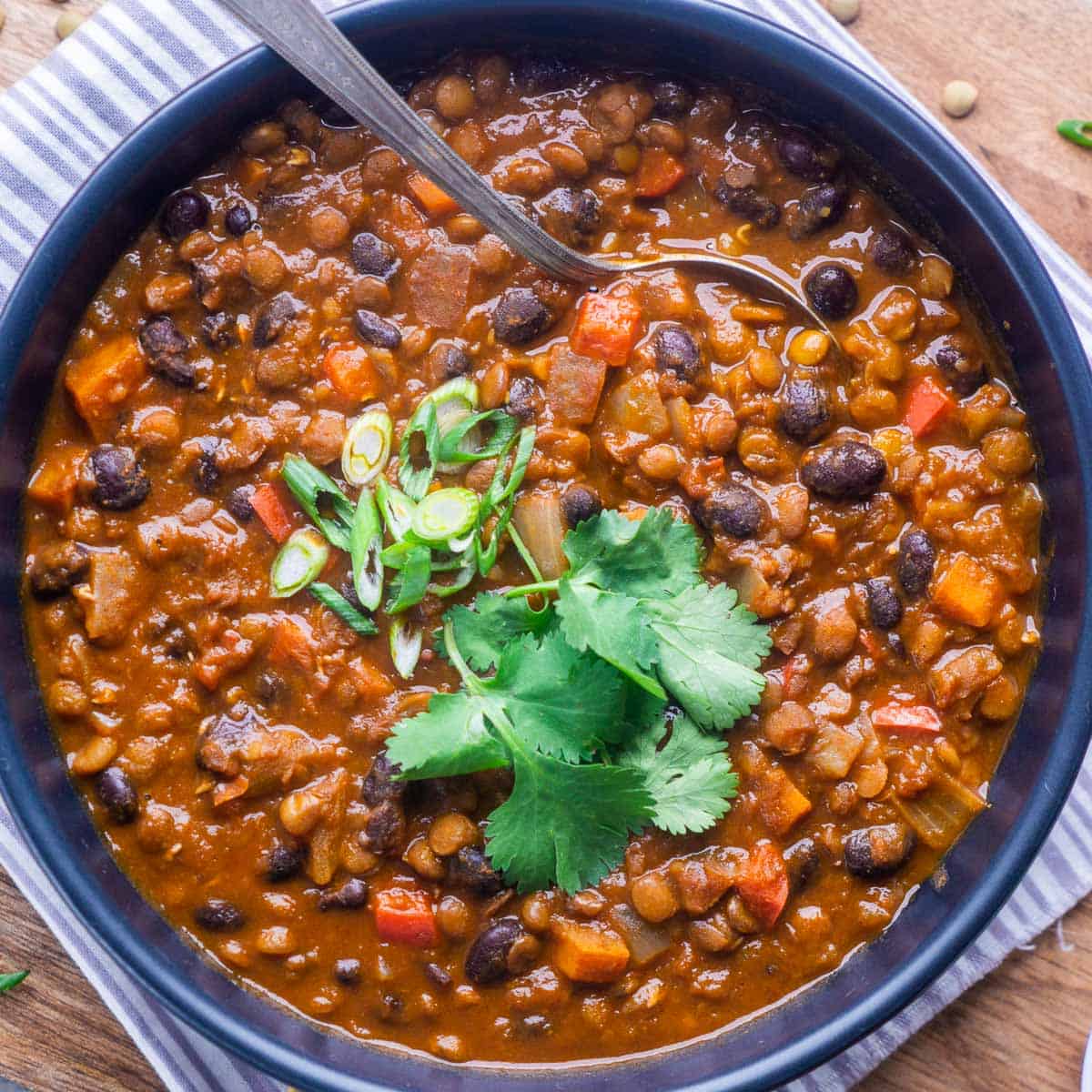 lentil chili in black bowl with fresh herb garnish and spoon