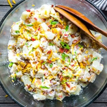 loaded potato salad in glass serving bowls with serving utensils