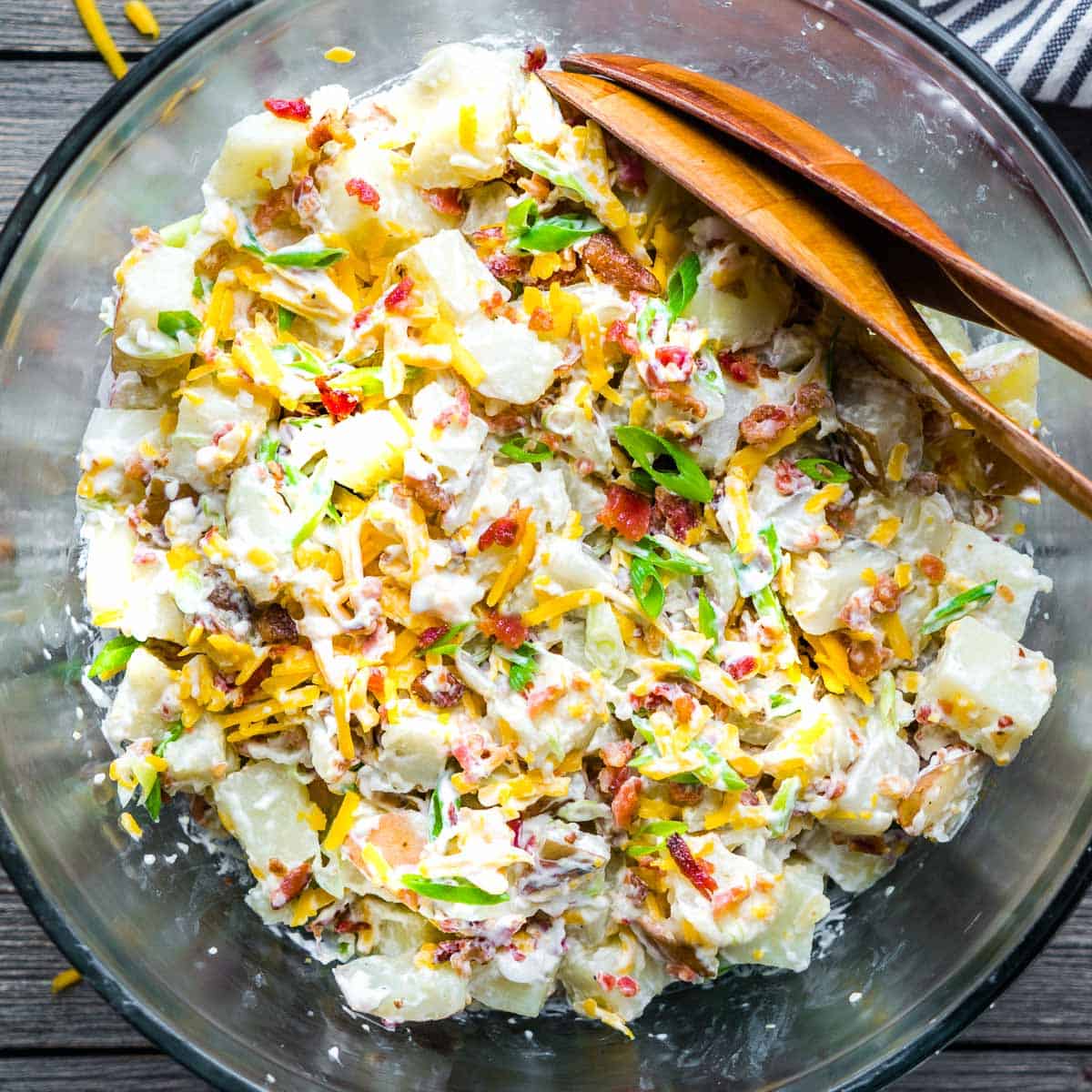 loaded potato salad in glass serving bowls with serving utensils