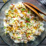 loaded potato salad in glass serving bowl with serving utensils
