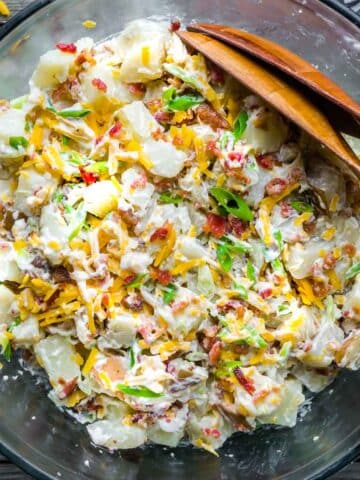 loaded potato salad in glass serving bowl with serving utensils