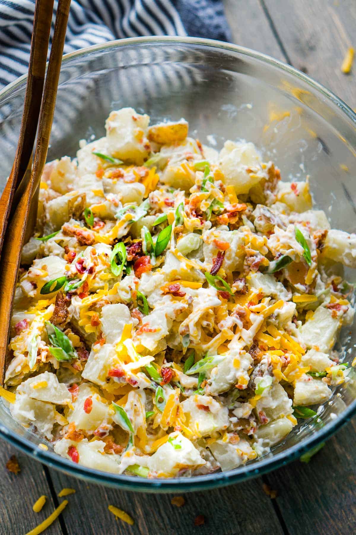 loaded baked potato salad in glass serving bowls with serving utensils