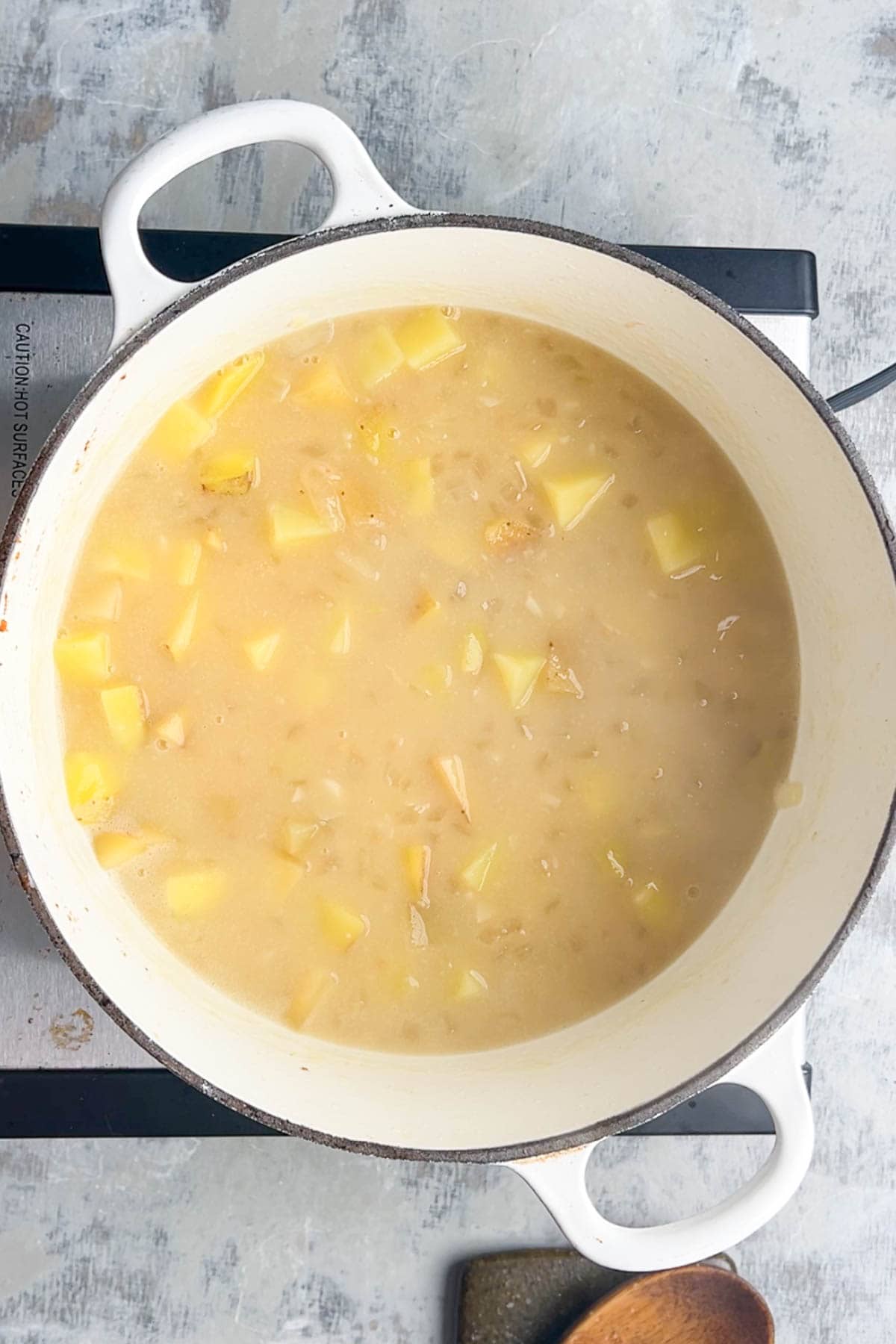 A white pot on a stove containing a simmering mixture of diced potatoes and broth.