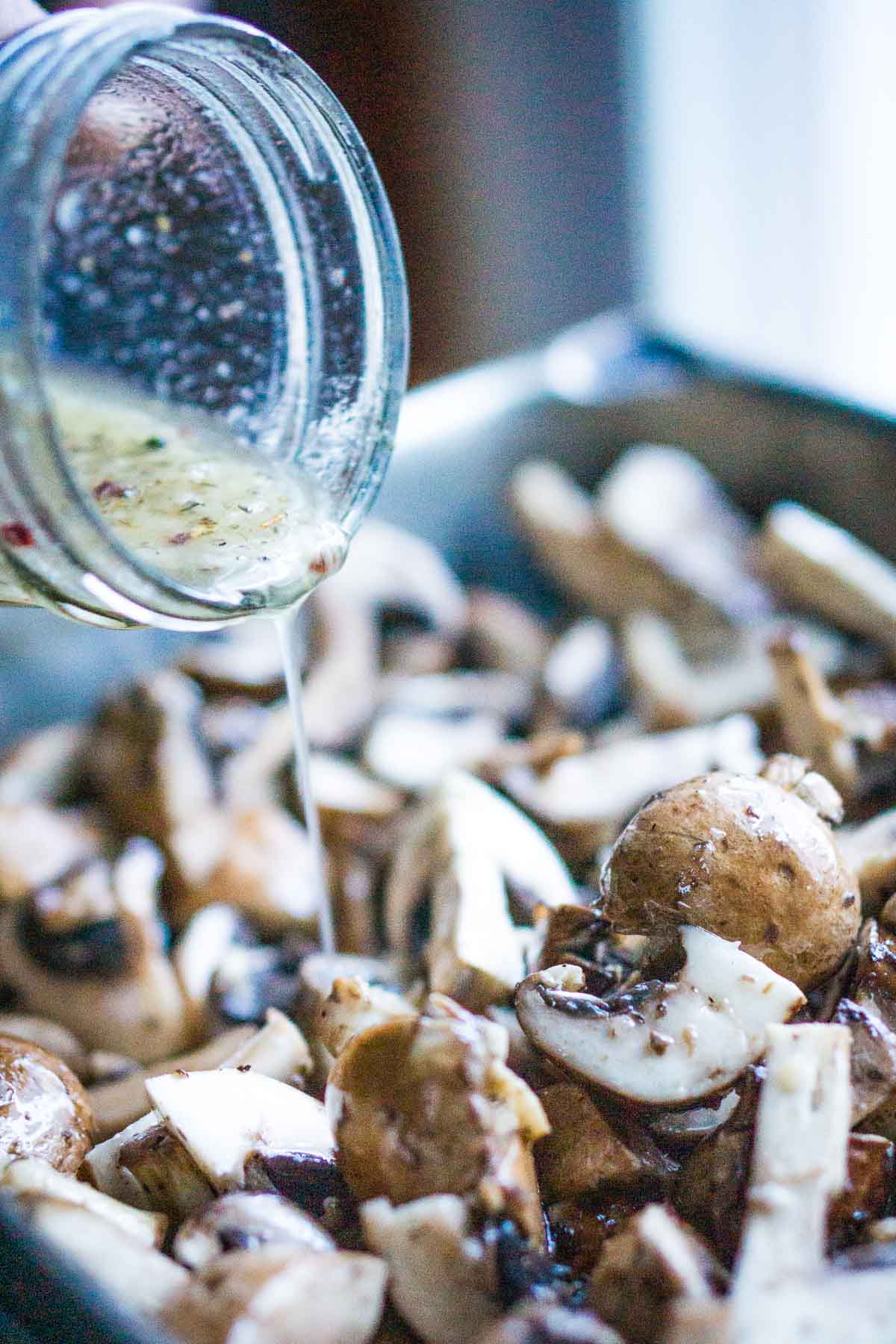 Italian dressing is poured into mushrooms in stainless steel pan