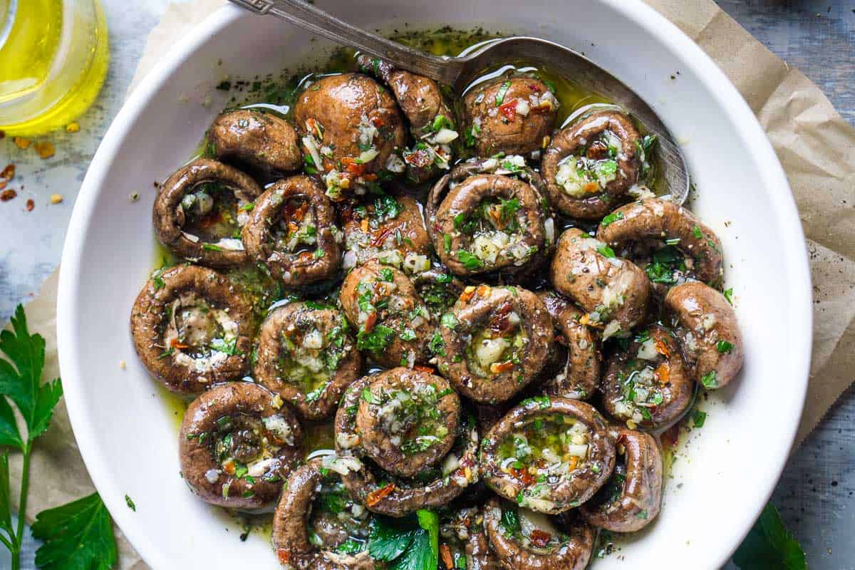 marinated mushrooms in white serving bowl with serving spoon