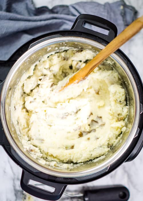 Mashed potatoes in instant pot with wooden spoon on marble background with grey towel