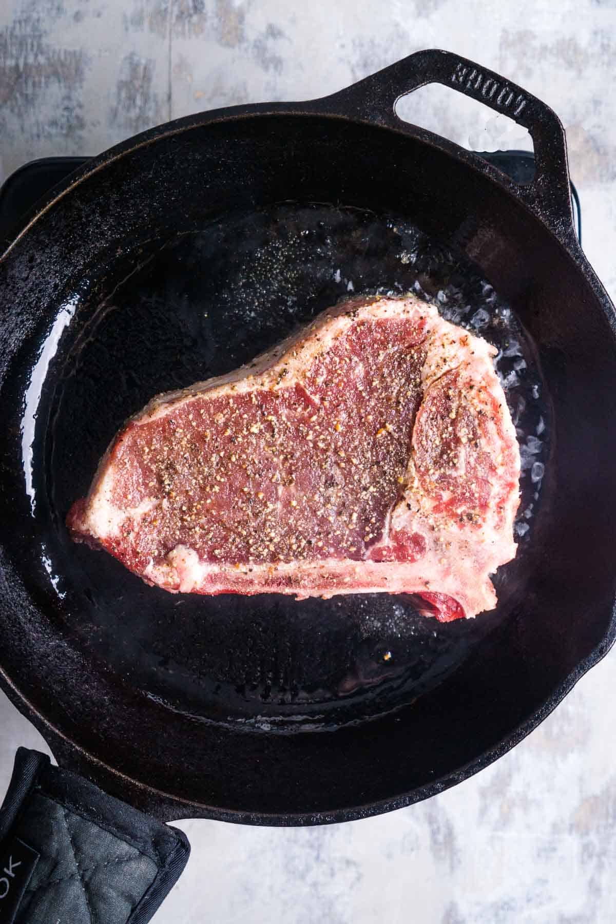 New York strip searing in layer of oil in cast iron skillet