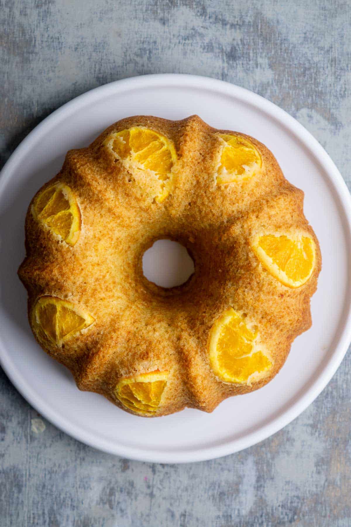Undecorated orange olive oil bundt cake on white plate.