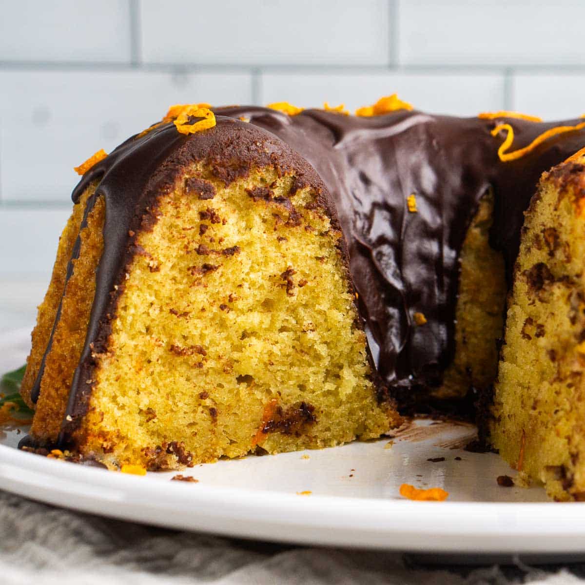 Close up side view of sliced orange olive oil cake with chocolate ganache topping.