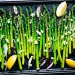 roasted asparagus on baking sheet with lemon wedges, shallots, and garlic