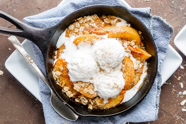 peach crisp topped with vanilla ice cream in iron skillet on blue linen-covered white plate on brown surface