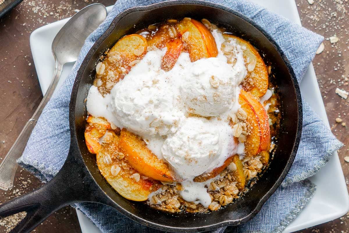 skillet peach crisp topped with scoops of vanilla ice cream
