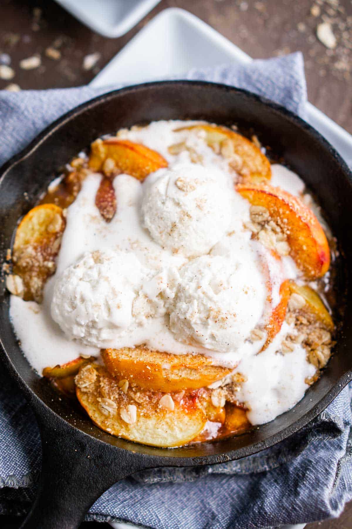 skillet peach crisp topped with scoops of vanilla ice cream