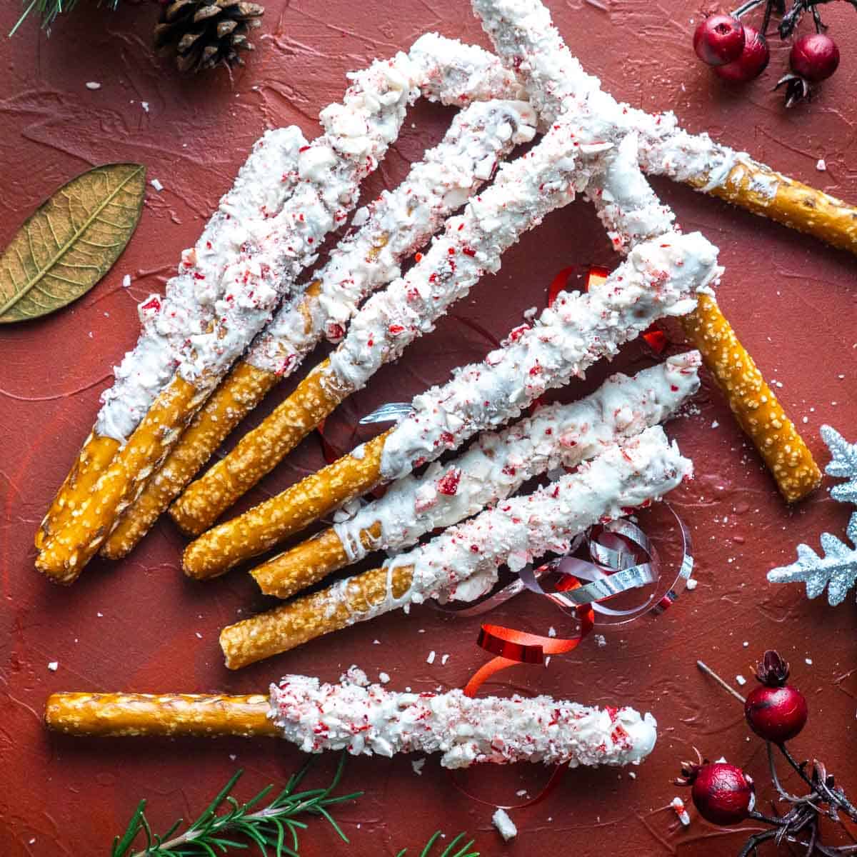 peppermint white chocolate pretzels laying on red background with scattered holiday decorations