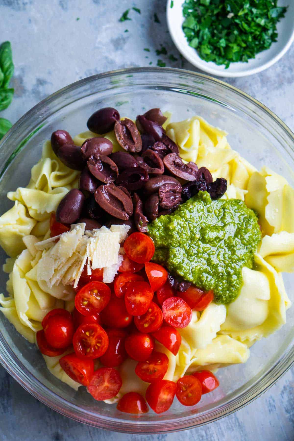 pesto tortellini pasta salad ingredients in glass bowl before tossing